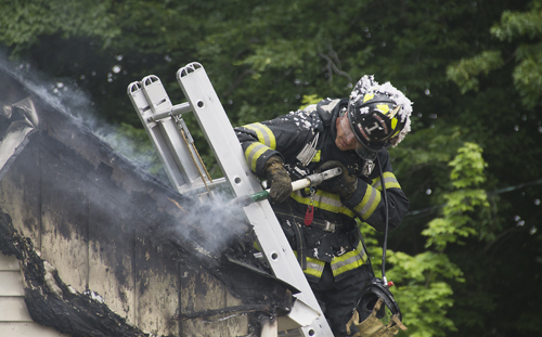 A Jamesport firefighter knocks away part of the charred roof at a fire on Herricks Lane Wednesday afternoon. (Credit: Paul Squire)