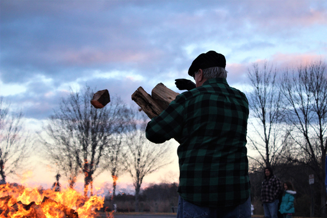 A man tosses another log into the fire. (Credit: Elizabeth Wagner)
