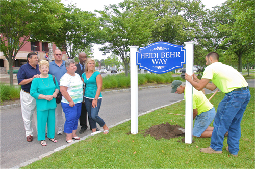 BARBARAELLEN KOCH PHOTO | HIghway department workers Ed Reeve (center) and Chris Bugee install a street sign Tuesday morning along the Peconic River in memory of fallen ambulance volunteer Heidi Behr, as the Behr family —  Heidi's grandmother Dorothy, mother June, father John and sister Dana look on. Jim Stark of the 'Heidi's Helping Angels' group and Highway Superintendent George 'Gio' Woodson were also on hand.