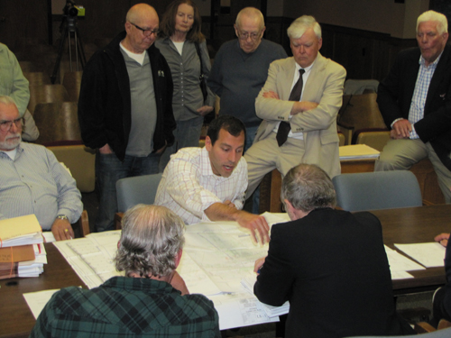 CAPTION: Haig Buchakjian, center, the Senior Vice President of Construction with Brixmor Property Group, promised to make things better at the Costco/Shops at Riverhead development at Thursday's Riverhead Planning Board meeting, while some of the neighbors who have been angered by that development look over his shoulder.