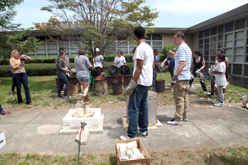 Students placing their art work in a container filled with burning paper. 