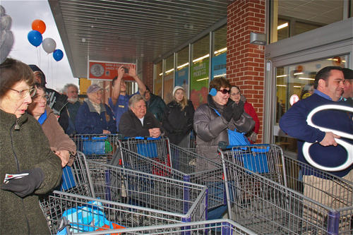 BARBARAELLEN KOCH PHOTO | Store manager (far right) Christopher Marinos cuts the ribbon as customers waited outside Friday morning.