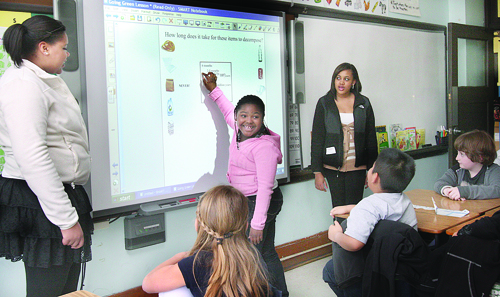Laniece Hutley steps up to the smart board to help answer the question 'How long does it take for these items to decompose?' during a presentation by Riverhead High School Key Club members D'Aja Mitchner (left) and Kailyn Gill to Kelly Cregan's third-grade class at Roanoke Avenue Elementary School Friday afternoon. D'Aja and Kailyn were teaching a 'Go Green Lesson to Save the Planet.'