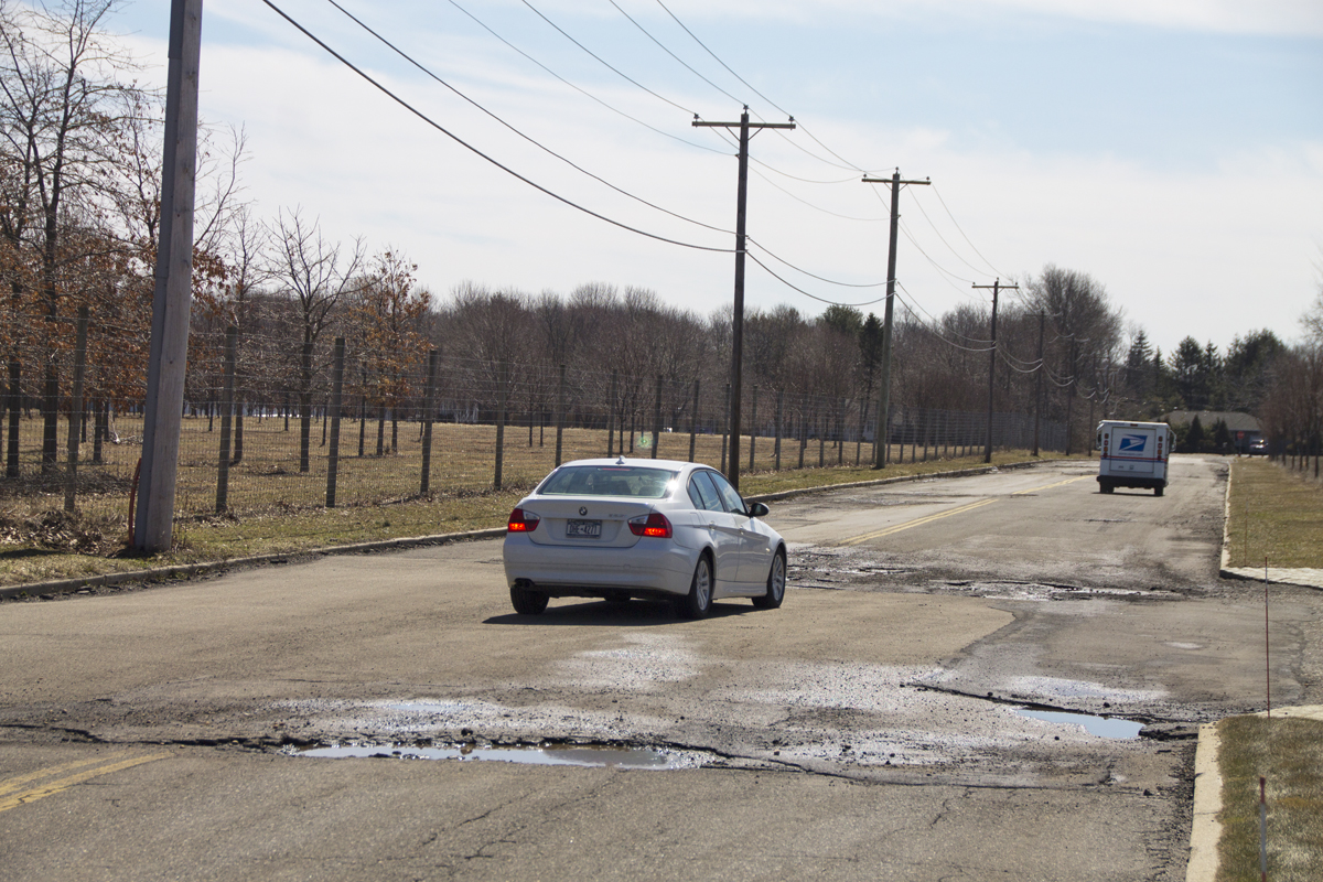Cars slow down to dodge potholes on Warner Drive in Calverton. (Credit: Paul Squire)