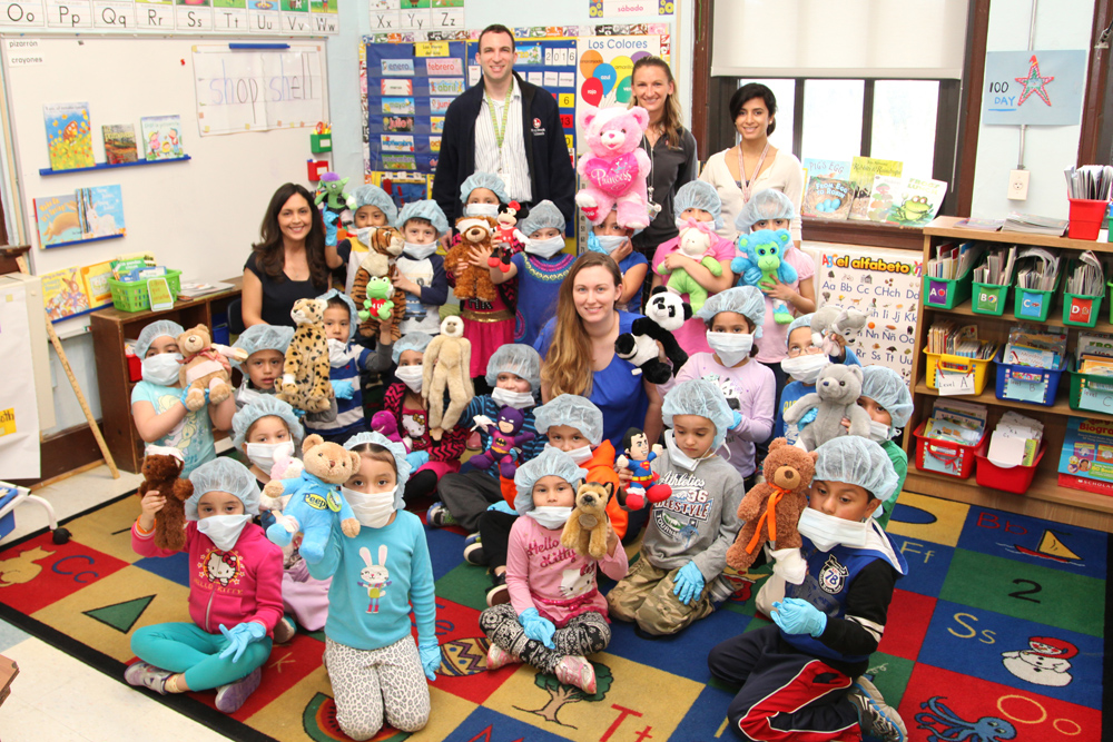 Kindergarten teacher Anselma Jimenez (seated far left with her students) and teacher assistant Marisa Mullane (middle in blue) with their kindergarten students. Also pictured in the back: L-R Dr. Noah Jablow, Kristi Landowski, MPH and Dr. Anupa Dalel from Stony Brook Trauma Center and Hospital.