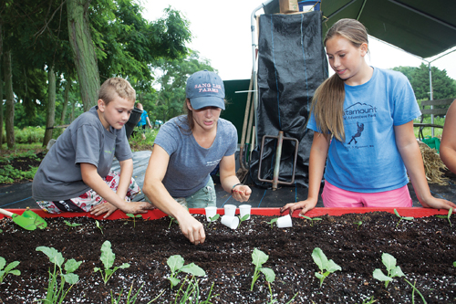 Young Farmers Camp coordinator Lucy Senesac plants seeds with Rudy Bruer, 10, of Mattituck and Julia Galasso, 12, of Westhampton. (Credit: Katharine Schroeder)