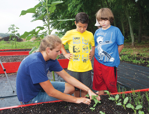 Teacher Kim Van Bourgondien demonstrates planting techniques to Jake Rosado, 7, of Miller Place, center, and Dylan Nolan, 8, of Cutchogue. (Credit: Katharine Schroeder)