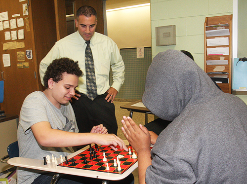 Dave Spinella watches as 10th graders Alek Lewis (left) and Xaviah Moore play a game of chess. (Credit: Barbaraellen Koch)