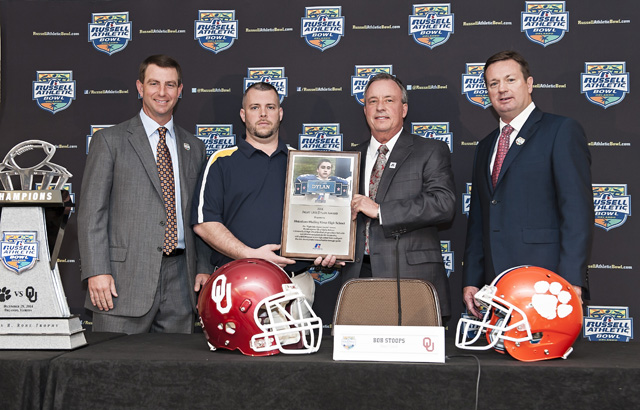 The 2014 Russell Athletic ‘Fight Like Dylan Award’ is presented to Shoreham-Wading River High School during the 2014 Russell Athletic Bowl Press Conference; L-R, Clemson University head coach Dabo Swinney; Russell Athletic senior vice president, general manager, Robby Davis; Shoreham-Wading High School assistant coach Tom Fabian; University of Oklahoma head coach Bob Stoops. (Credit: Russell Athletic, courtesy)