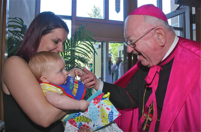 Bishop William Murphy gets friendly with Alyson Touhey of Pennsylvania and her 10-month-old son Killian before the graduation ceremony. (Credit: Barbaraellen Koch)