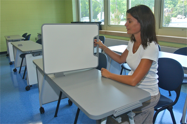 Social Studies teacher Kate Brown demonstrates how the desks in her classroom has white boards that can be use to take notes on or to set up as a divider during tests.