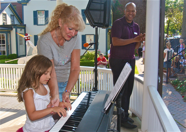East End Arts music student Lilah Caputo, 7, with teacher Andrea Modugno performing on the porch of the school as school director Shenole Latimer (right) watches. (Credit: Barbaraellen Koch)