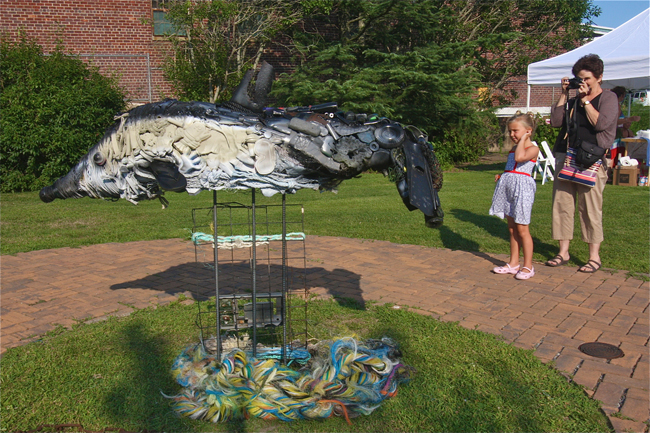 Carol Janickey of Holtsville, with granddaughter Chloe Howard of Center Moriches, photographs a dolphin sculpture by artist Carolyn Munaco of Hampton Bays made of discarded plastic found on the beaches. (Credit: Barbaraellen Koch)