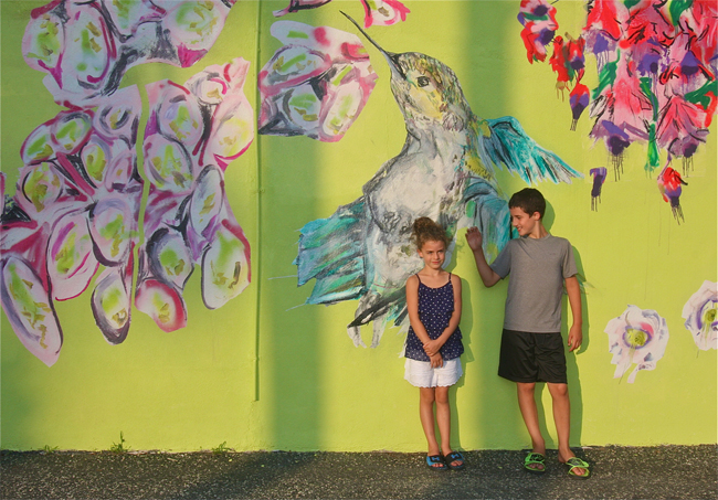 Kate Oliver, 6 and brother Ryan, 9, of Riverhead posed for a photo at "The Garden Party" mural by Caitlyn Shea on the corner of McDermott Street and East Main Street. (Credit: Barbaraellen Koch)