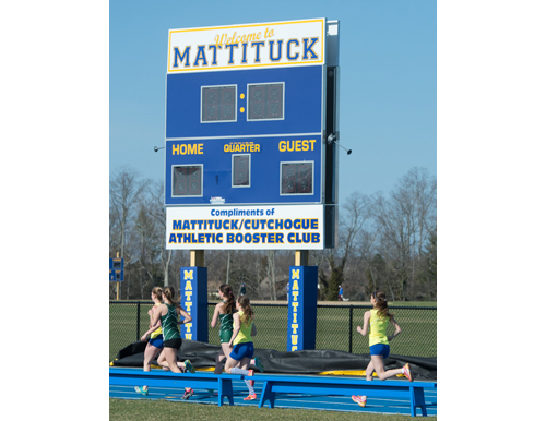 Runners in the 1,500-meter race pass the scoreboard near Mattituck's new track on Monday. (Credit: Robert O'Rourk)