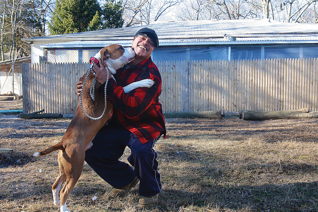 Kent Animal Shelter kennel manager Ricky Appling gets some kisses Friday from Yogi, a year-old pit bull mix, in the Calverton shelter's play yard. (Credit: Barbaraellen Koch)