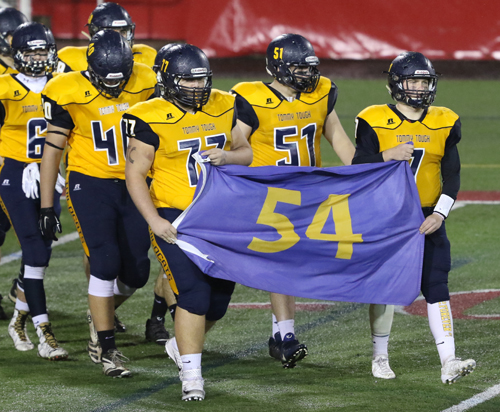 James Puckey, left, and Kevin Cutinella carry the 54 flag in memory of Tom Cutinella onto the field before Shoreham-Wading River's win over Elwood/John Glenn in the Suffolk County Division IV final. (Credit: Daniel De Mato, file)