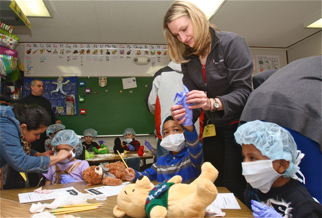 Ms. Ladowski helps Jaiveon Lee put on protective medical gear before examining his teddy bear, Nick.